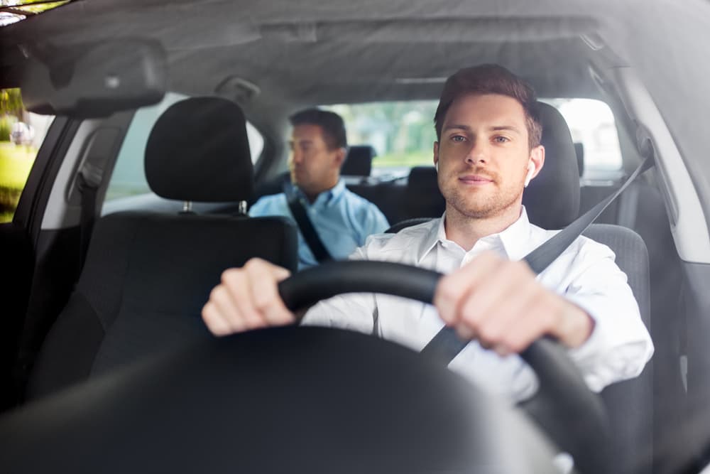 In the domain of transportation, the scene unfolds with a male driver using wireless earphones or a hands-free device, steering his vehicle with a passenger alongside him.