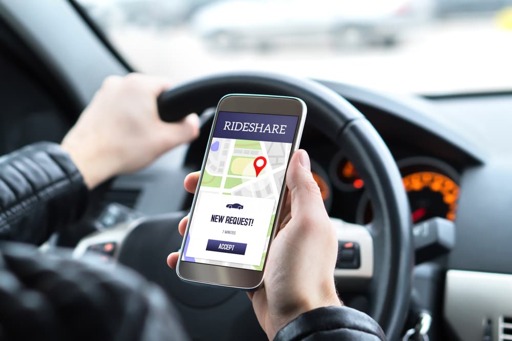 A rideshare driver is behind the wheel, navigating through the rideshare app on their mobile phone. Suddenly, a new taxi ride request pops up on the screen.