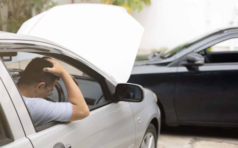 A man, who is the driver, holding his head near a broken car on the road after a car accident.