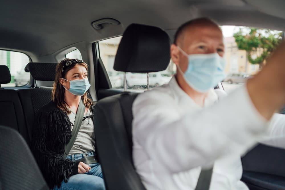 A taxi driver wearing a mask with a masked passenger in the back seat.