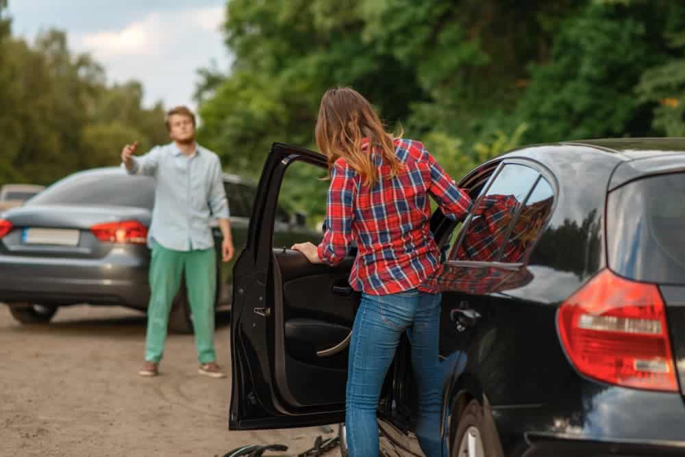 A male and female driver standing near their cars on the road after a car accident.