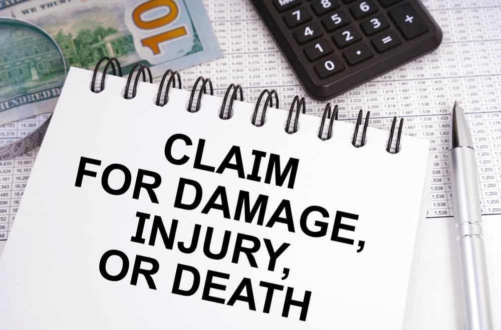 On the table, there is money, a calculator, and a notebook with the inscription "Claim for Damage, Injury, or Death."