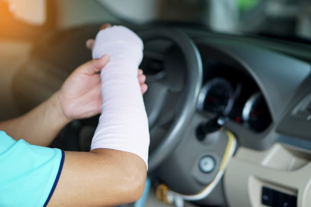 Unsafe driving: An injured man with a bandage on his hand and arm is driving a car, which might cause an accident due to the discomfort of driving in this condition.