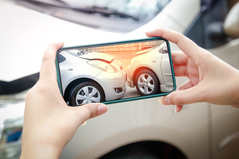 A person taking a photo of a car accident scene with a smartphone, capturing two damaged cars.