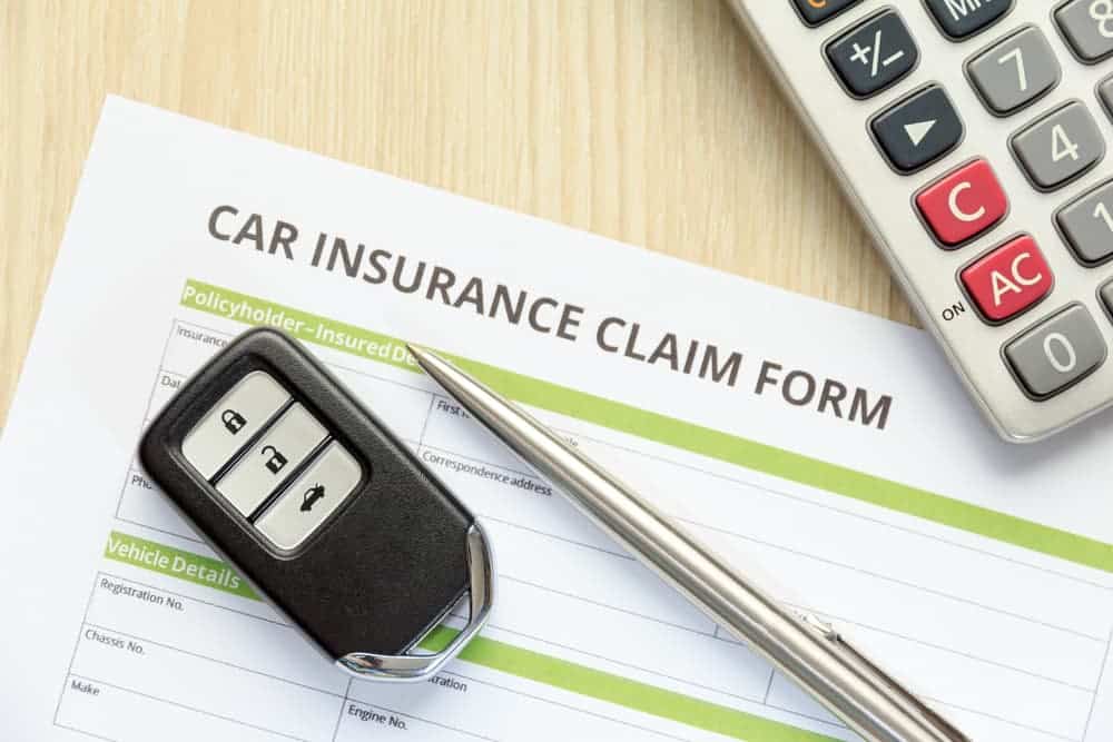 A car insurance claim form with a car key, a pen, and a calculator placed on top.