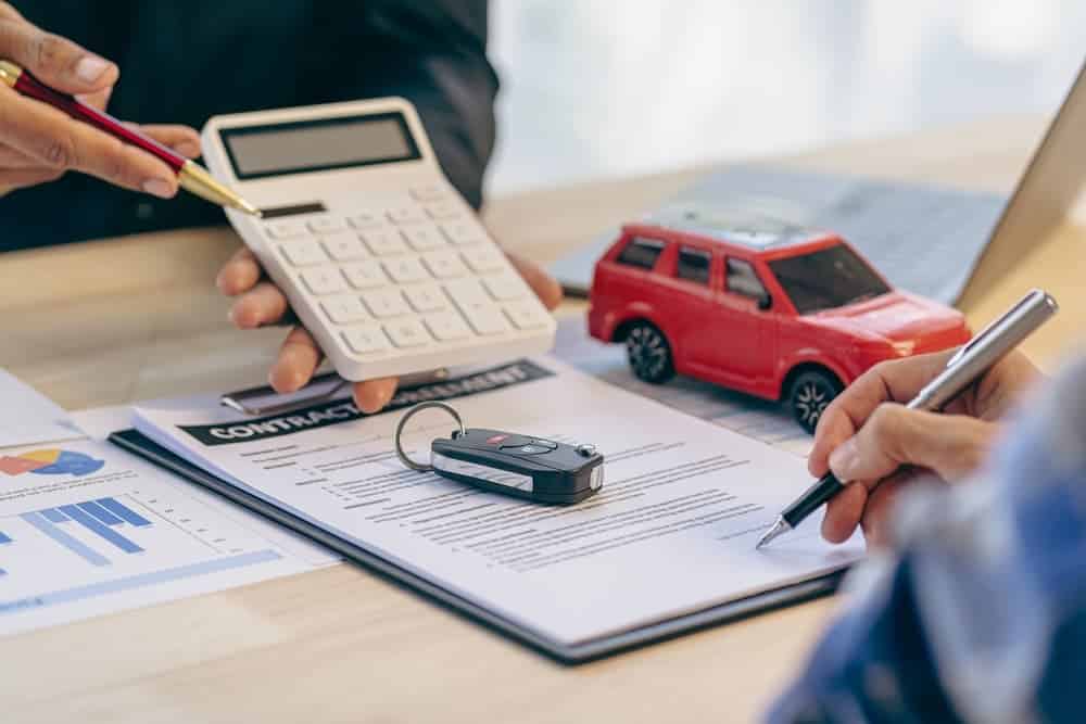 Two people reviewing contract papers, one holding a calculator, with a car key and toy car.
