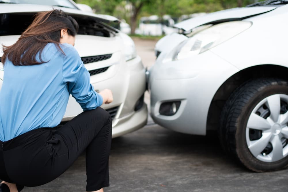 A woman driver looks sad after a car accident, feeling distressed due to the lack of car accident insurance to cover the damages.