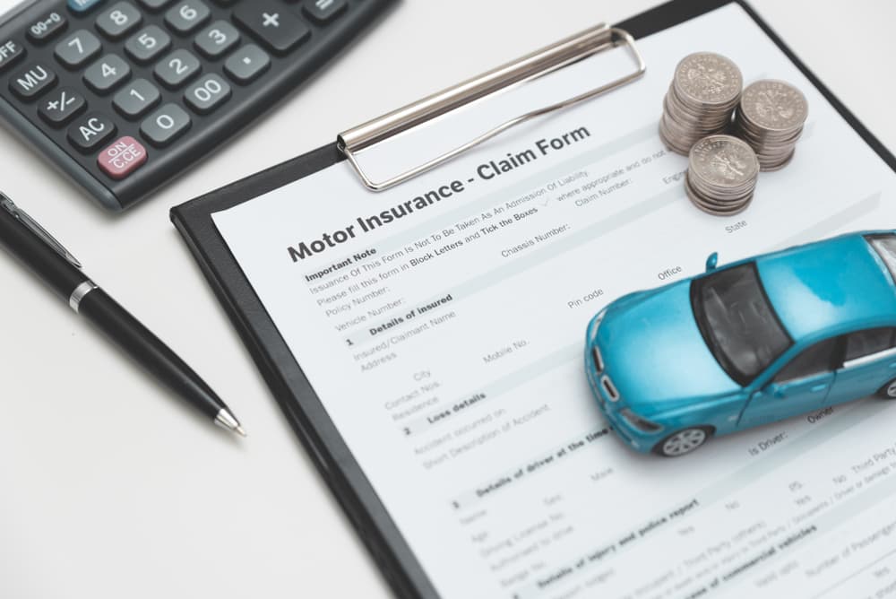 Car insurance claim form with coin stack, calculator, and model car.